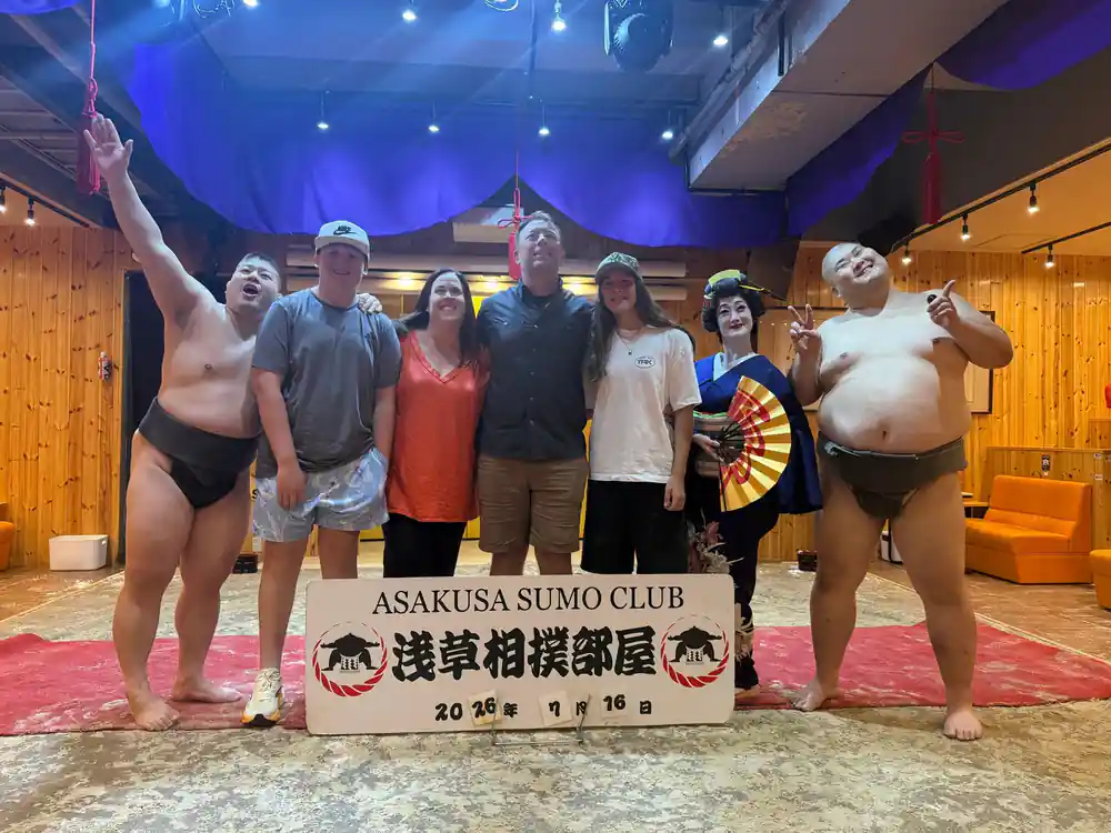 Group of sumo wrestlers and visitors posing with banner