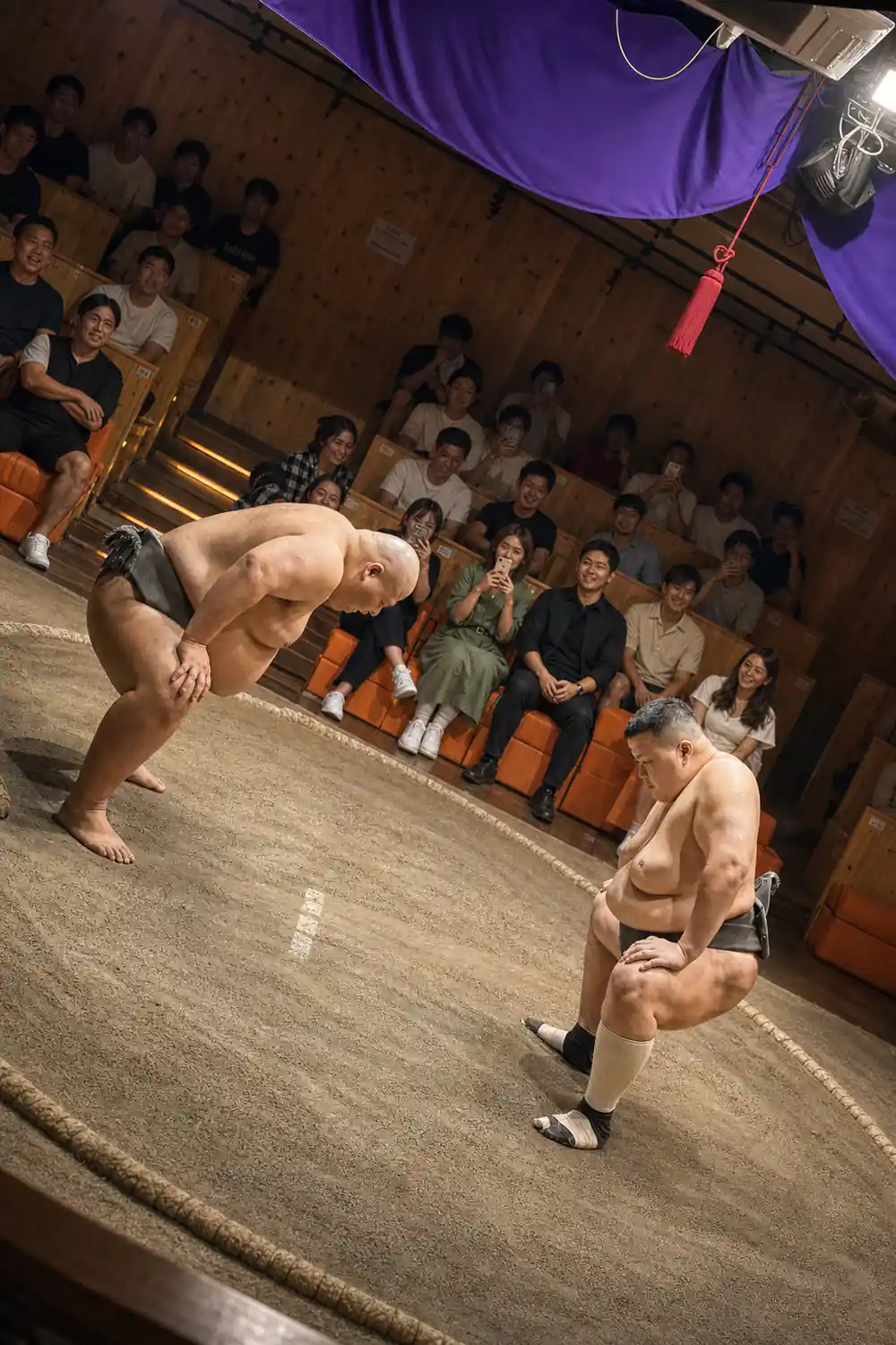 Two sumo wrestlers competing in indoor arena with audience