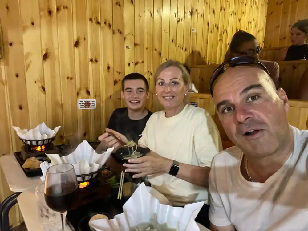 Three people at wooden table with food and beverages