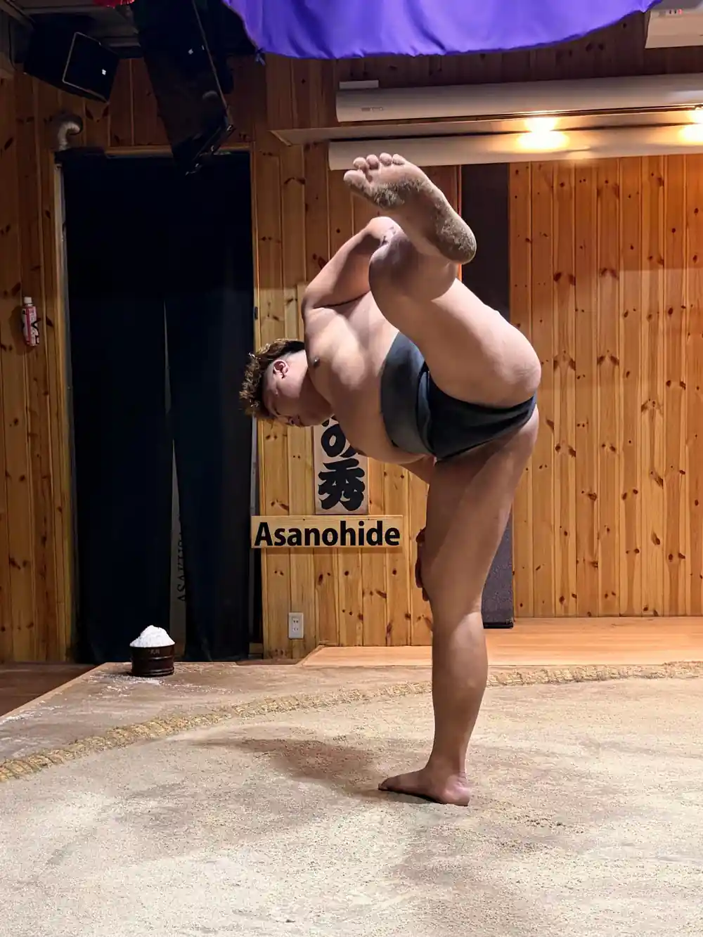 Sumo wrestler performing handstand pose on sand ring