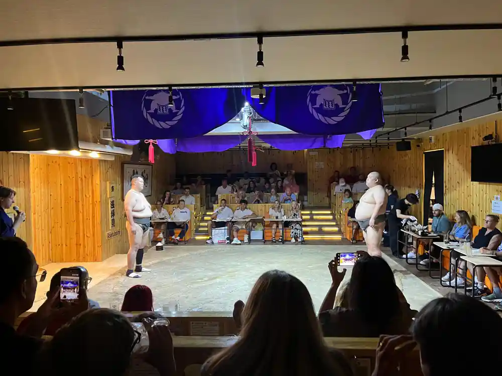 Sumo wrestlers posing with spectators in traditional hall