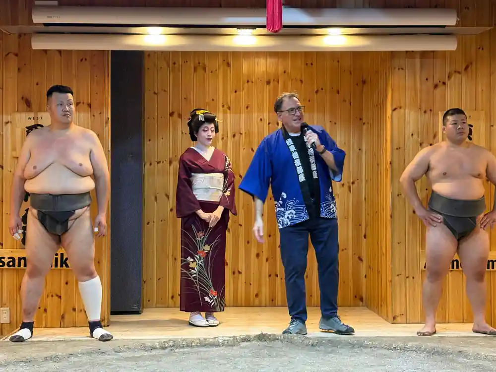 Sumo wrestlers posing with woman and man indoors