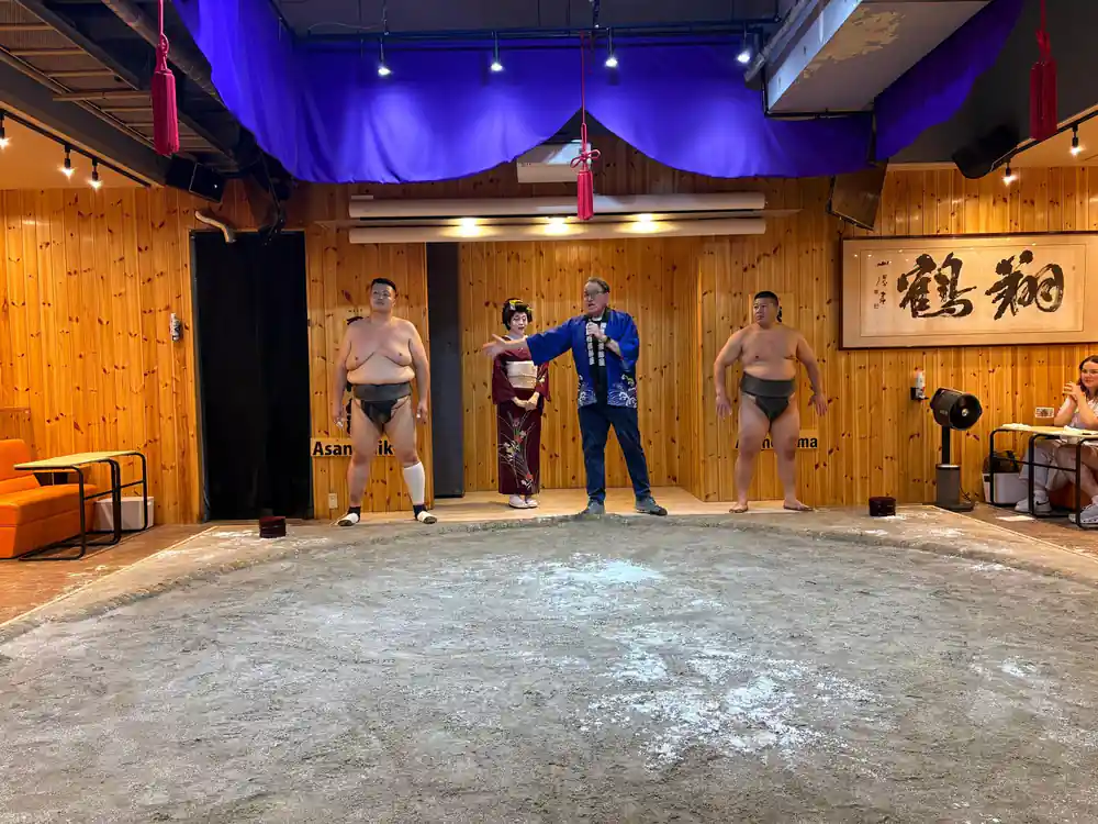Sumo wrestlers and woman in traditional dress indoors