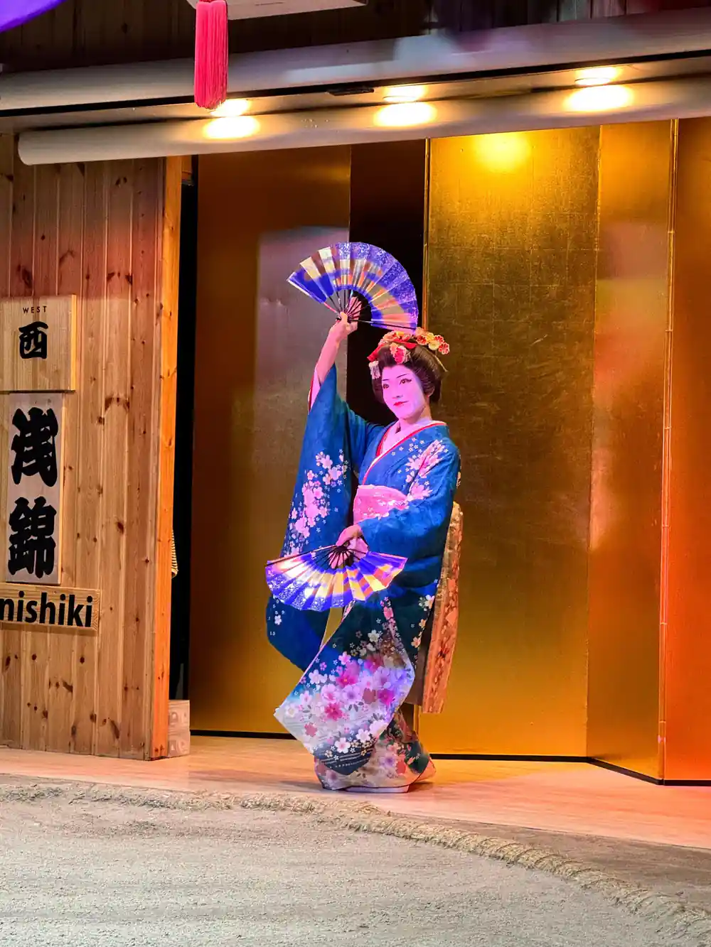 Woman in blue and pink kimono with decorative fan outside